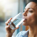 Keep calm and hydrate on. Shot of a woman drinking a glass of water at home.